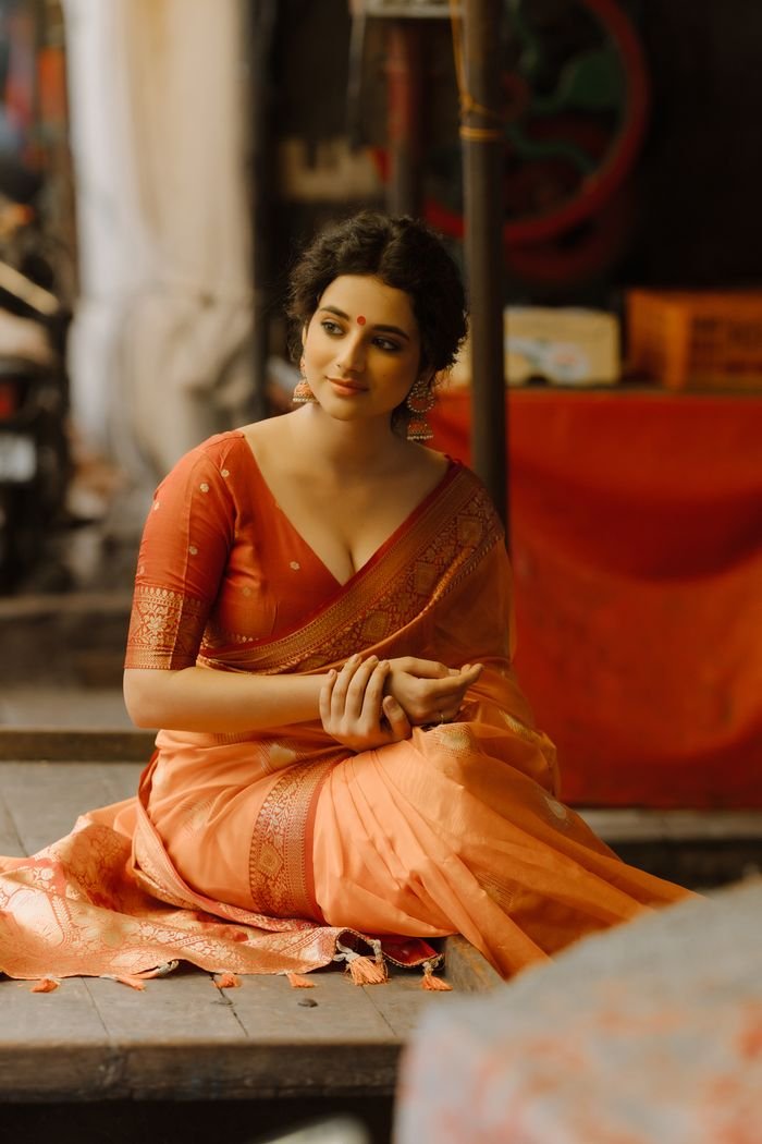 collection-02 A woman in a traditional orange sari, sitting gracefully indoors with a serene expression.