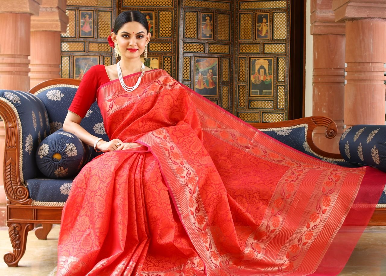 hero-img Woman in red saree poses elegantly indoors, highlighting traditional fashion and culture.