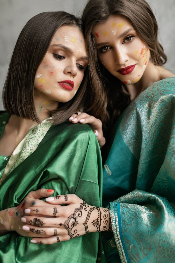 collection-05 Two women in green sarees adorned with henna and Holi powder, posing elegantly.